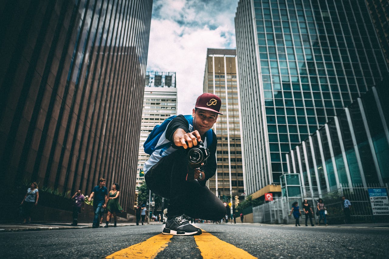 amenities A young man with a camera kneels on a bustling city street, surrounded by skyscrapers.